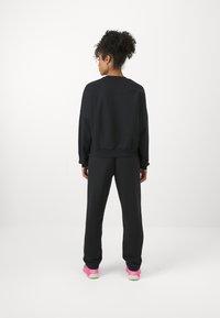 Μαύρη μπλούζα και σετ φόρμας με ταιριαστά παντελόνια. Μαλακό ύφασμα με χαλαρή εφαρμογή. Σημαντικά ροζ παπούτσια με κίτρινες λεπτομέρειες.