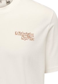 Camiseta de algodón blanca con "Midnight Spritz" bordado en un tipo de letra contorneada en marrón en la parte izquierda del pecho; con cuello redondo y mangas cortas.