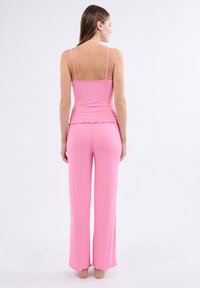 Haut rose à côtes avec des fines bretelles, associé à un pantalon rosé évasé avec un ourlet en festons. Texture lisse et design ajusté.