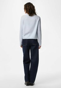 Ljusblå stickad tröja med ribbad mudd och vågig nederkant, kombinerad med mörk denim vidbyxor och svarta skor. Bakvy.