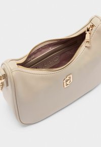 Borsa a tracolla in pelle beige con hardware dorato, chiusura a zip e una texture liscia; l'interno è foderato con un motivo stampato in logo.