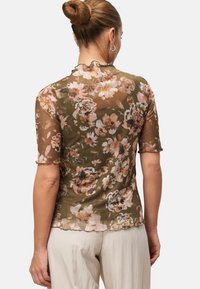 Sheer olive green top featuring a floral pattern in pink and peach tones, short sleeves with scalloped edges, and a fitted silhouette.