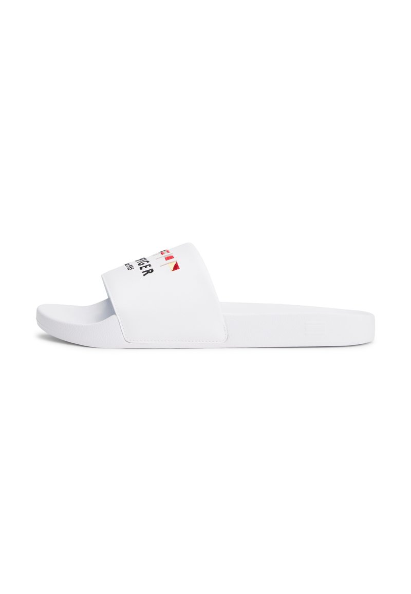 Hvit sandaler med åpen tå, bred stropp med flaggdesign og svart tekst på toppen, flat såle, sidevisning.