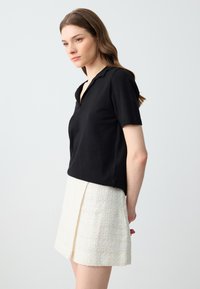 Haut noir à manches courtes de style polo, en tissu tricoté, associé à une mini-jupe blanche texturée avec un léger pli et un ourlet effiloché.