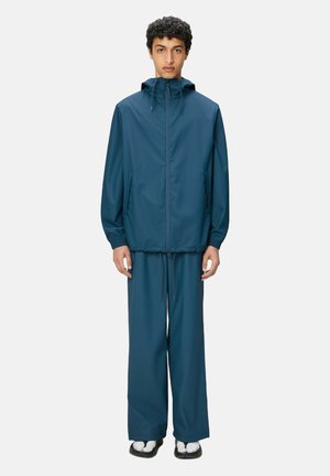 Chaqueta con capucha y pantalones a juego en color verde azulado oscuro, resistentes al agua. Cuenta con puños elásticos, bolsillos laterales y un cordón ajustable en la cintura.