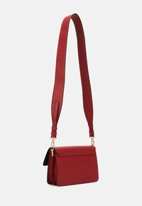 Borsa a tracolla in pelle rossa con ampia tracolla regolabile e chiusure in tonalità dorata, mostrata su uno sfondo bianco semplice.