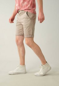 Shorts beige clair avec ourlets retroussés, poches latérales et fermeture à bouton, accompagnés de baskets montantes blanches.