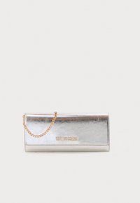 Borso in metallo argento di Love Moschino con tracolla in oro e logo embossato sul davanti su sfondo bianco.