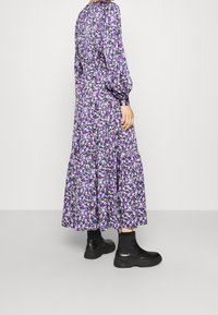 Fialové šaty s květinovým potiskem, dlouhými rukávy a volánkovou sukní. V kombinaci s černými kotníkovými botami. Hladká tkanina s volným designem.