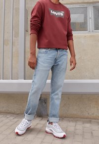 Sudadera roja con el logo de "Levi's", jeans de color azul claro y zapatillas blancas con acentos rojos. Conjunto casual con los puños de los jeans enrollados.