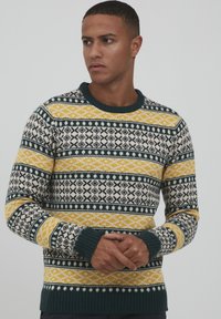 Pulover din lã tricotat cu dungi modelate în nuanțe de navy, galben și crem. Prezintă un decolteu și manșete ribjate, precum și motive geometrice în întreaga țesătură.