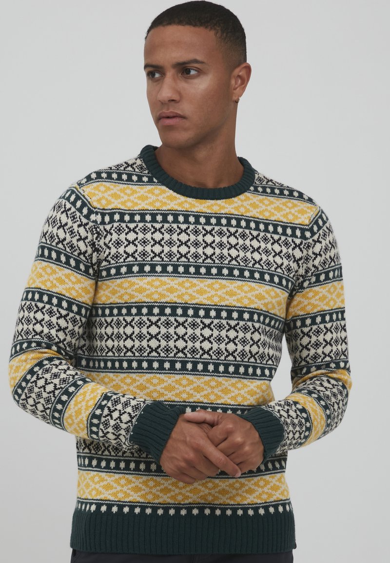 Pull en tricot avec des rayures à motifs bleu marine, jaune et crème. Il possède un col et des poignets côtelés, ainsi que des motifs géométriques sur l'ensemble.