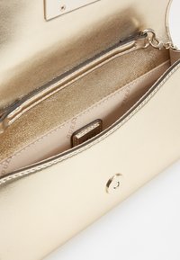 Intérieur de sac à main métallique doré présentant une texture lisse, une poche zippée et une étiquette de marque à l'intérieur d'une doublure beige.