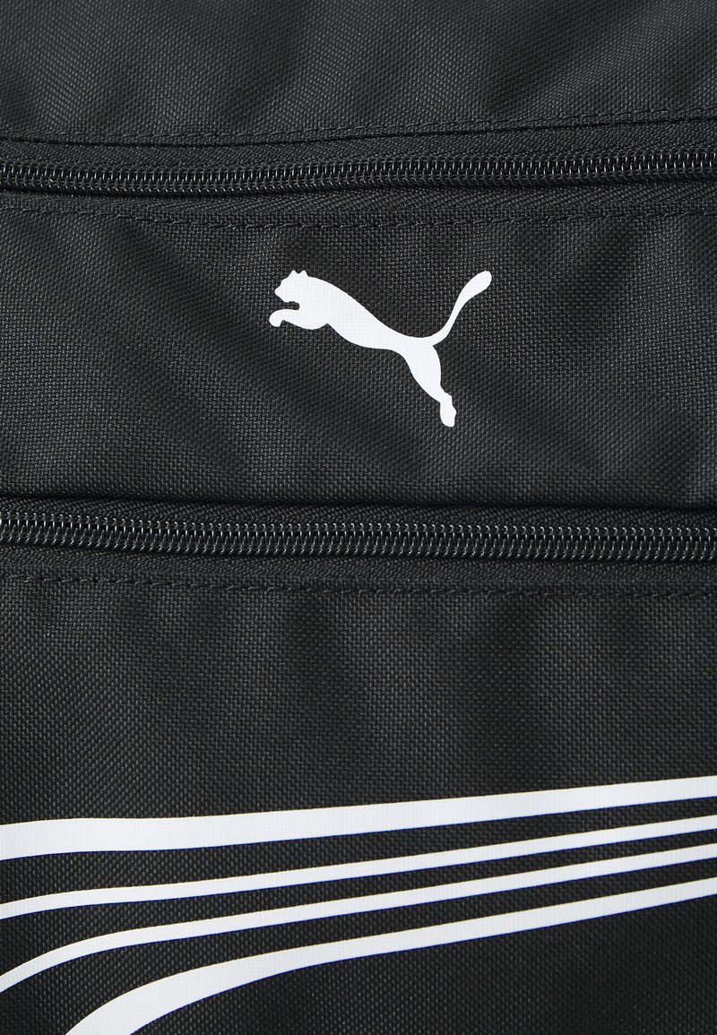 Sac en tissu noir avec un logo Puma blanc, une fermeture éclair lisse et des rayures blanches diagonales sur le devant. La texture est durable et mate.