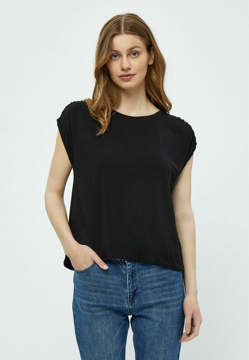 Top nero a maniche corte con vestibilità rilassata e scollo rotondo, realizzato in tessuto liscio. Abbinato a jeans in denim azzurro chiaro.