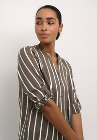 Camisa de botones color caqui con rayas verticales blancas, de tela ligera, con mangas enrolladas y diseño de cuello en forma de V.
