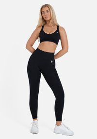 Schwarzes Sport-BH- und Leggings-Set aus dehnbarem Material, mit einer figurbetonten Passform, glatter Textur und einem kleinen Logo-Akzent am Bund.