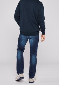 Suéter azul marino de cuello redondo, combinado con jeans de denim de lavado medio. Los zapatos son blancos con acentos rojos y azules. Textura suave en toda la prenda.