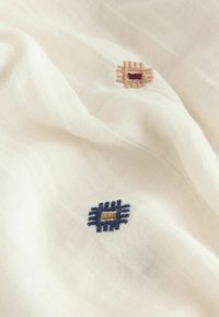 Cream fabric with a delicate texture features two embroidered square patterns: one in beige and brown, the other in navy blue with a beige center.