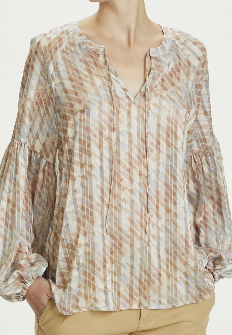 Blusa leggera e multicolore con scollo a V, maniche a palloncino e un motivo a diamante nei toni del beige, blu e marrone. Texture morbida.