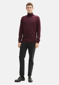 Burgundowy sweter z golfem wykonany z miękkiego materiału, w połączeniu z czarnymi spodniami i czarnymi sznurowanymi butami. Prosty design, dopasowany krój.