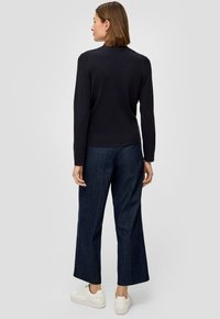 Czarny top z długim rękawem w połączeniu z szerokimi ciemnoniebieskimi dżinsami i białymi sneakersami. Stylizacja ma dopasowaną sylwetkę i casualowy design.