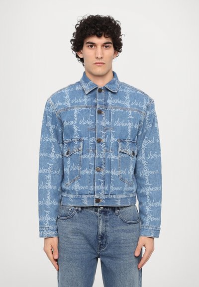 Denim jacket in light blue with a repetitive white script pattern. Features two chest pockets, button closure, and a classic collar. Fitted design.