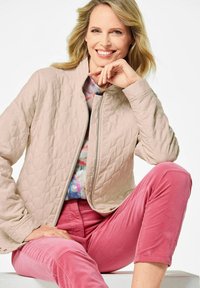 Gequilte, lichtbeige jas met een ritsluiting en staande kraag, gecombineerd met roze corduroy broek. Zachte stof en gestructureerd patroon.