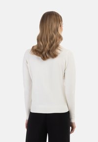 Vaaleanbeige neulepaita, jossa on pitkät hihat, ribbaustyyliset hihansuut ja helma, sileä pinta, asetettu yksinkertaista taustaa vasten.