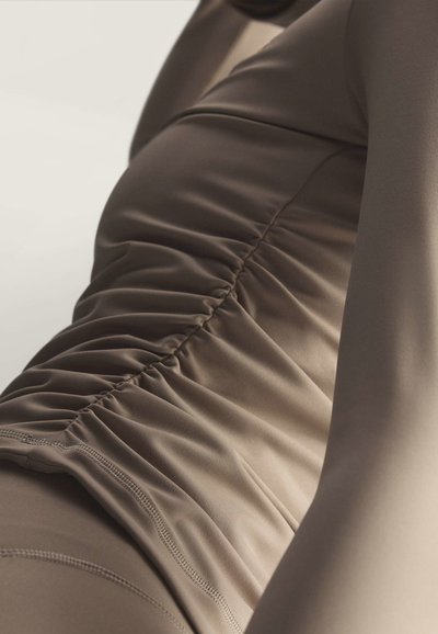 Close-up of a person wearing fitted brown ruched fabric clothing, showing texture and stretching across the torso and arm.