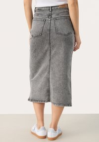 Sivá denim midi sukňa so rovný strihom, dvoma zadnými vreckami a surovým lemom, kombinovaná s bielymi teniskami s svetlomodrými akcentmi.