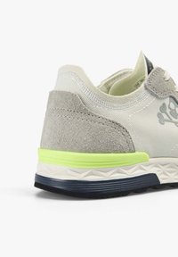 Vue arrière d'une chaussure de sport en daim blanc et gris avec une semelle à motif noir et vert néon sur fond blanc uni.