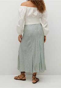 Witte off-the-shoulder top met pofmouwen, gecombineerd met een groene rok met bloemenpatroon. Bruine sandalen met bandjes zichtbaar.