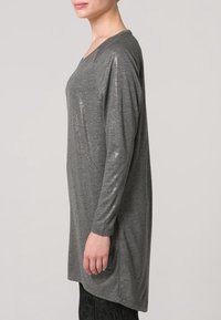 Šedá dlouhý rukáv tunika z měkkého materiálu s jemným lesklým vzhledem. Má široký výstřih a volný střih, sahající do poloviny stehen.