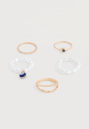 Viis kuldset ja pärlikujulist sõrmust, millest üks valgete helmeste ja sinise silmamotiiviga, on eksponeeritud heledal taustal.