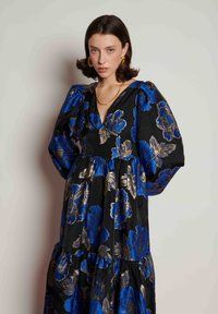 Μαύρο φόρεμα με μπλε και χρυσό λουλουδάτο σχέδιο, μανίκια φουσκωτά, λαιμόκοψη V και στρωματοποιημένη σχεδίαση. Υφασμάτινη υφή που προσθέτει βάθος.