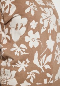 Tessuto a maglia marrone con un motivo floreale bianco, caratterizzato da fiori e foglie di varie dimensioni e forme. Texture liscia con leggero allungamento.