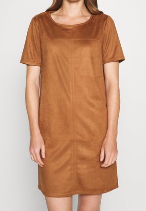 Kobieta ubrana w krótką sukienkę zamszową koloru wielbłądziego o długości do kolan, z okrągłym dekoltem i widocznymi detalami szwów.