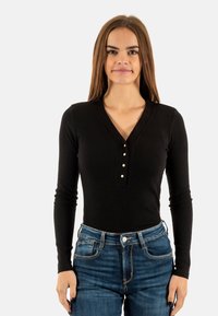 Bodysuit noir à manches longues côtelé avec un décolleté en V et quatre boutons, associé à un jean en denim bleu taille haute.
