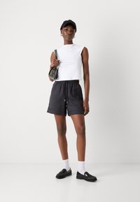 Top bianco senza maniche, pantaloni corti neri con coulisse, scarpe slip-on nere, calzini bianchi e un cappellino nero. Design minimalista con texture morbide.