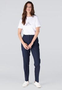 Witte t-shirt met een grijze graphic, gecombineerd met marineblauwe gestreepte broek en witte sneakers. De outfit heeft een relaxte pasvorm en een zachte stof.