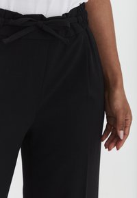 Zwarte broek met elastische tailleband en een gestrikt strikdetail, gemaakt van gladde stof en voorzien van zijzakken voor een casual pasvorm.