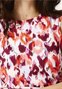 Materiał w wielokolorowy kwiatowy wzór w odcieniach czerwieni, różu i fioletu, o fakturowanej powierzchni i miękkim układzie. Okrągły dekolt.