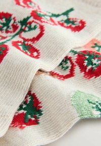 Knitted sweater fabric with cream base, featuring red and green holiday patterns, including trees and swirls, with a soft texture.