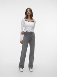 Haut à manches longues blanc avec un bord noir le long de l'encolure carrée, associé à un jean large taille haute gris clair et des baskets blanches.