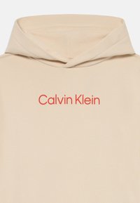 Felpa con cappuccio in tessuto beige chiaro, caratterizzata da un logo rosso "Calvin Klein" sul davanti, con una texture liscia e una vestibilità comoda.
