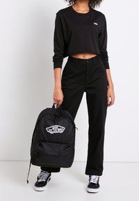 Musta Vans-reppu logolla, kangasmateriaali, säädettävät hihnat, etutasku, yhdistettynä mustaan lyhythihaiseen toppiin ja housuihin.