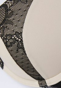 Sutien bej cu dantelă neagră la margini, cu cupe netede și un design structurat. Dantela are un model floral, adăugând textură și detaliu.