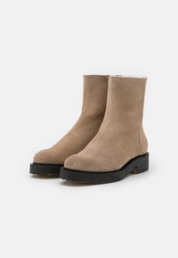 Botines de ante beige con punta redondeada, que presentan una suela de plataforma negra texturizada y un forro suave en la parte superior del eje.