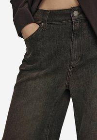 Jean en denim bleu foncé avec une coupe droite, présentant des coutures visibles, une fermeture à bouton métallique et des poches latérales profondes.